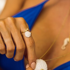 Può includere: Una collana d'oro con un ciondolo a forma di riccio di mare bianco e una pietra preziosa blu. Il ciondolo è circondato da piccole stelle dorate. La collana è indossata da una persona che indossa un costume da bagno blu.