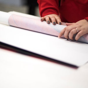 Peut inclure: Une personne roule un papier blanc et rose &agrave; motifs sur une surface blanche.