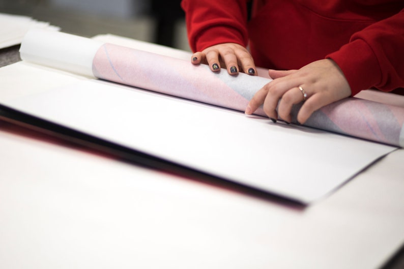 Peut inclure: Une personne roule un papier blanc et rose &agrave; motifs sur une surface blanche.