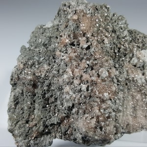 May include: A rough, grey rock with a vein of pink crystals. The crystals are small and clustered together. The rock has a natural, unpolished look.