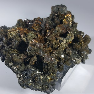 Könnte beinhalten: Ein Cluster aus dunkelgrauen und goldenen Kristallen mit einer rauen, strukturierten Oberfläche. Die Kristalle sind in einem zufälligen, organischen Muster angeordnet.