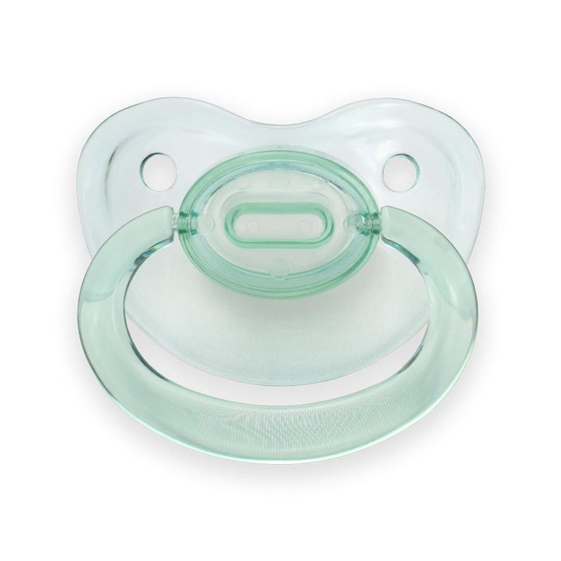 May include: A green pacifier with a clear shield and a handle. The pacifier is made of silicone and is designed for babies.