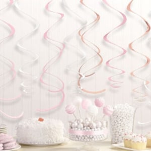 Könnte beinhalten: Eine festliche Szene mit hängenden rosa, weißen und roségoldenen Luftschlangen. Ein weißer Kuchen mit Zuckerguss, Cake Pops, Cupcakes und eine Tüte weiße Süßigkeiten sind auf einem Tisch mit Tellern und Makronen arrangiert.