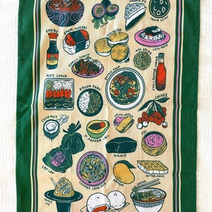 Puede incluir: Un paño de cocina beige con un borde verde que presenta ilustraciones coloridas de la cocina hawaiana, incluyendo poke, spam musubi y shave ice. El paño tiene varias ilustraciones de comida.