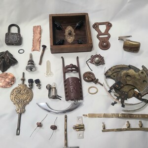 May include: A collection of antique metal and wooden hardware components, including a padlock, decorative escutcheons, gears, and a small wooden box with decorative elements. Various colors and textures are visible.
