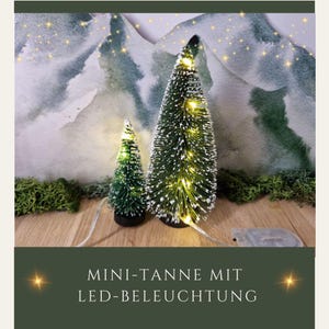 Könnte beinhalten: Zwei künstliche Mini-Weihnachtsbäume mit weißen, flockigen Zweigen und warmweißen LED-Lichtern. Der größere Baum ist etwa 30 cm hoch und der kleinere Baum ist etwa 15 cm hoch. Die Bäume stehen auf einer Holzoberfläche mit einem grünen Moos-Hintergrund.