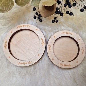 Könnte beinhalten: Zwei Untersetzer aus Holz mit natürlicher Holzoptik. Die Untersetzer haben ein dekoratives Design aus Sternen und grünen Zweigen am Rand.