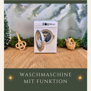 May include: A miniature white washing machine with the door open, revealing the drum. The machine has silver accents and is set on a wooden surface. The text "WASCHMASCHINE MIT FUNKTION" is at the bottom of the image.