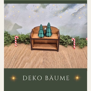 Könnte beinhalten: Zwei teal Weihnachtsbaumdekorationen mit Sternakzenten sitzen auf einer kleinen Holzbank. Die Bank steht auf einer Holzoberfläche, mit Zuckerstangen und Grünzeug im Hintergrund. Der Text "DEKO BÄUME" steht unten.