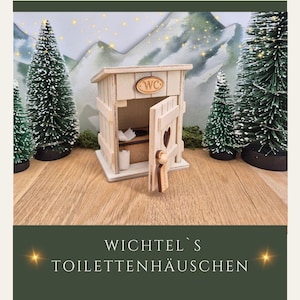 Puede incluir: Un pequeño retrete de madera con una puerta abierta, que revela un pequeño interior. El retrete tiene un recorte en forma de corazón en la puerta y un letrero de "WC". El texto "WICHTEL'S TOILETTENHÄUSCHEN" está en la parte inferior.