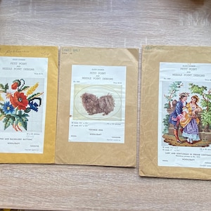 May include: Three vintage Petit Point needlepoint design kits. The kits feature floral, dog, and romantic couple designs. Each kit is in a tan paper envelope with printed text and a color image of the finished needlepoint.