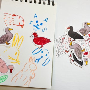 May include: A sheet of paper with drawings of a cat, a dog, and a rabbit. There are also several stickers of ducks in various colors and patterns.