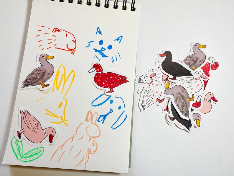 May include: A sheet of paper with drawings of a cat, a dog, and a rabbit. There are also several stickers of ducks in various colors and patterns.