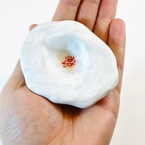 May include: White ceramic dish with a deep indentation in the center. The dish has a red stamp with the text "RD" in the center of the indentation.