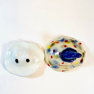 May include: Two ceramic figurines, one white with black eyes and the other with a blue hat and colorful polka dots.