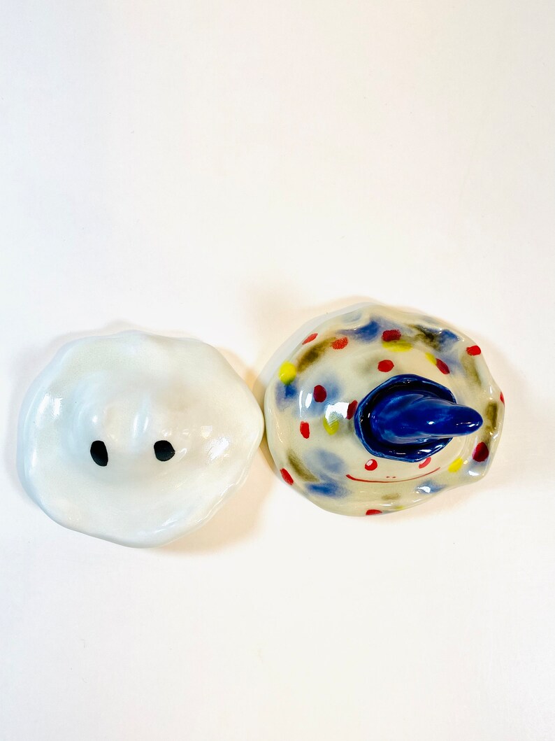 May include: Two ceramic figurines, one white with black eyes and the other with a blue hat and colorful polka dots.