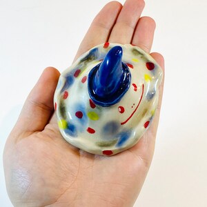 May include: A ceramic figurine with a blue hat and colorful polka dots. The figurine has a whimsical, cartoon-like appearance.