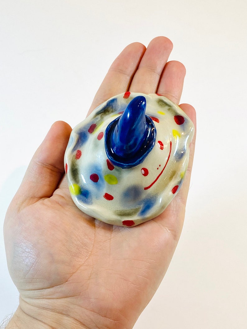 May include: A ceramic figurine with a blue hat and colorful polka dots. The figurine has a whimsical, cartoon-like appearance.