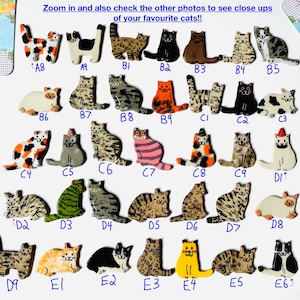 May include: A collection of small, flat, cat-shaped ceramic pins or ornaments, each labeled with a unique alphanumeric code. The cats feature various colors, patterns, and markings, including solid black, orange, tabby, calico, and spotted designs.