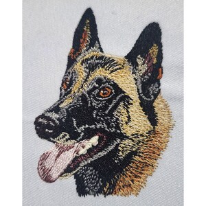 May include: Embroidered portrait of a Belgian Malinois dog. The dog's head is rendered in detailed stitching, showcasing a black muzzle, tan and black fur, and brown eyes. The dog's tongue is pink, and the background is white.