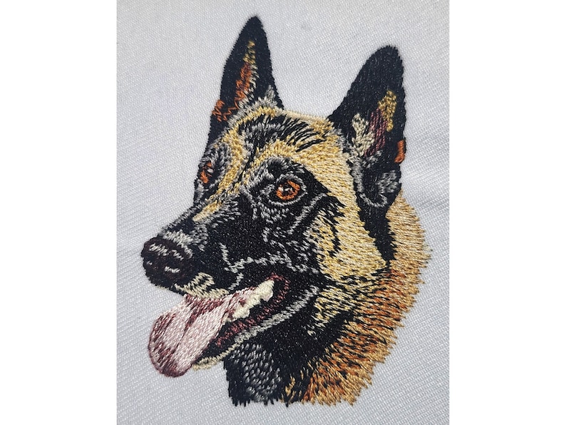 May include: Embroidered portrait of a Belgian Malinois dog. The dog's head is rendered in detailed stitching, showcasing a black muzzle, tan and black fur, and brown eyes. The dog's tongue is pink, and the background is white.