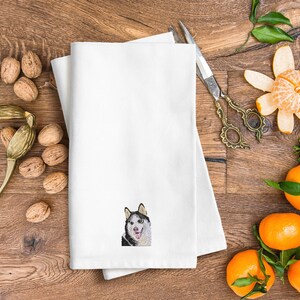 May include: White kitchen towel with a black and white embroidered image of a husky dog.