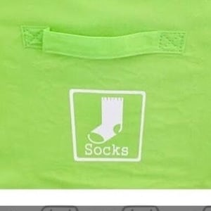 May include: Green canvas laundry basket with a white label that says "Socks".  The basket has a handle on the top.  Below the basket are nine labels with icons and text for different types of clothing: Short Sleeve, Socks, Shorts, Underwear, Tank Tops, Pants, Long Sleeve, Pajamas, and Sweaters.