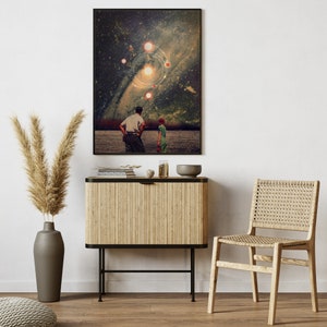 May include: A framed print of a surrealist collage featuring two figures standing in a field, looking up at a swirling galaxy with multiple stars and planets. The print is displayed on a wooden cabinet with a woven chair in the foreground.