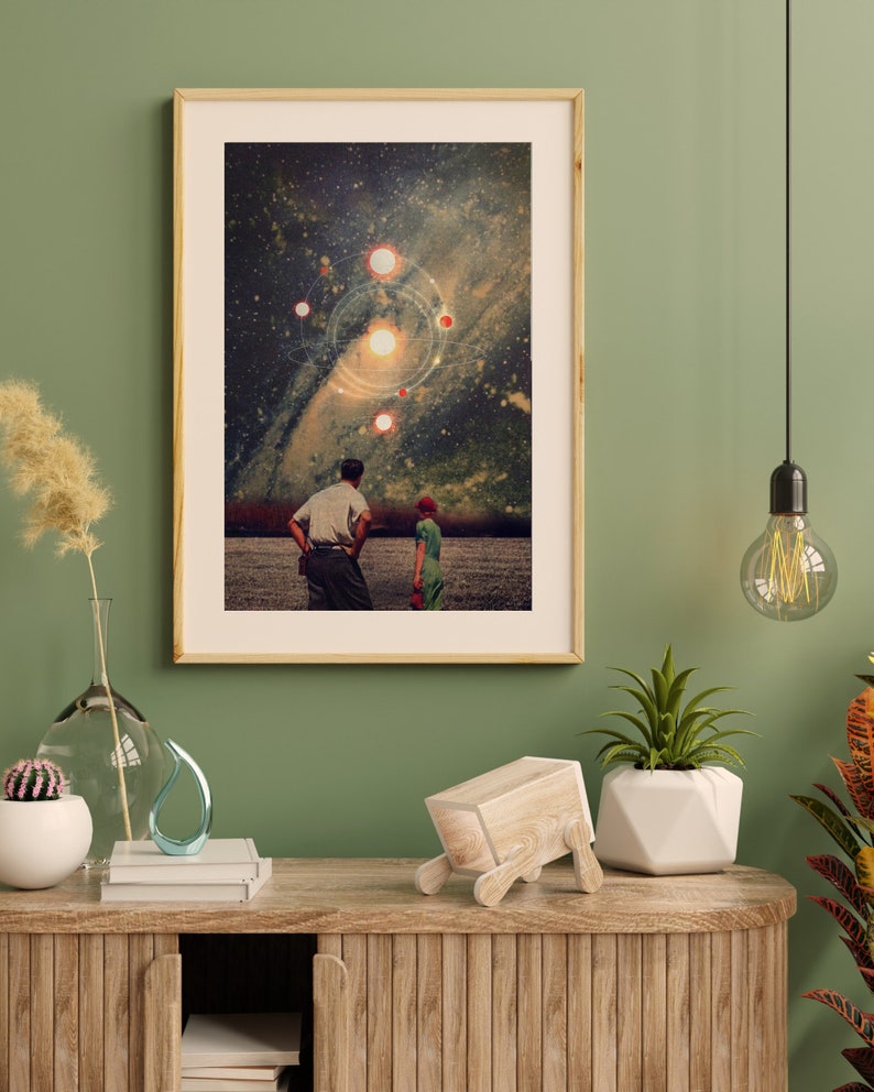 May include: A framed collage art print featuring a couple standing in a field, looking up at a starry night sky with a galaxy and planets. The print has a vintage aesthetic.