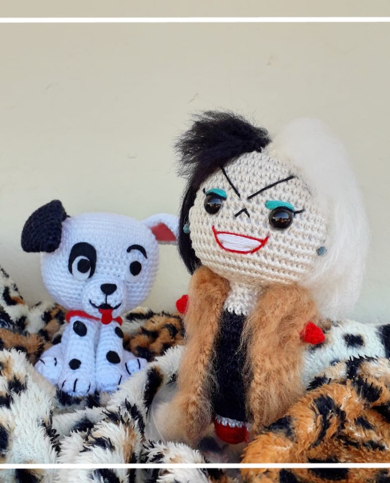 Op de afbeelding: Een gehaakt pluche speelgoed van Cruella de Vil uit de Disney-film 101 Dalmati&euml;rs. Ze draagt een bruine bontjas en heeft zwart en wit haar. Ze houdt een gehaakt pluche speelgoed van een Dalmati&euml;r puppy vast.