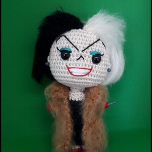 Op de afbeelding: Een gehaakte pop van Cruella de Vil uit de Disney-film 101 Dalmati&euml;rs. De pop heeft zwart en wit haar, een rode glimlach en draagt een bruine bontjas.