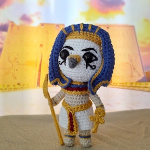 May include: A crocheted amigurumi toy of an Egyptian pharaoh wearing a blue and gold headdress, holding a gold staff and a golden ankh.