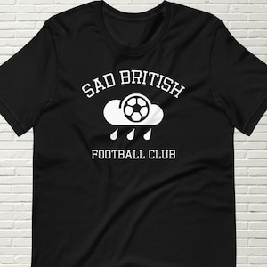 May include: Black t-shirt with a white graphic of a cloud with a soccer ball inside and rain drops falling. The text "SAD BRITISH FOOTBALL CLUB" is written above and below the graphic.