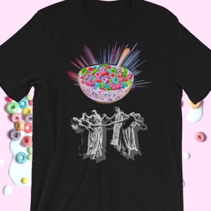 Puede incluir: Una camiseta negra con un gráfico de un tazón de cereal colorido con una cuchara, rodeado de una explosión de luz. Debajo del tazón, cinco figuras bailan en círculo.