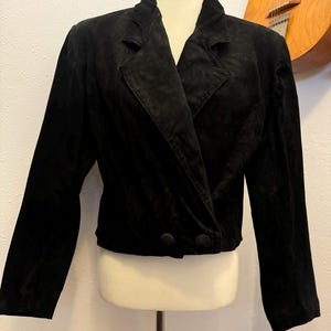 May include: A black suede jacket with a long sleeve and a single button closure. The jacket has a collar and a lapel.