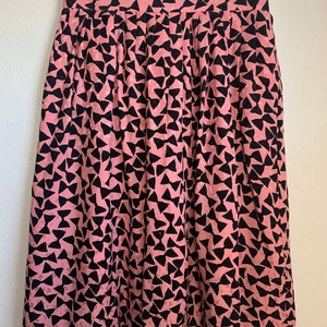 May include: A pink midi skirt with a black bow print. The skirt has a pleated design and a high waist.
