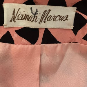 May include: A white label with the text "Neiman-Marcus" in brown lettering. The label is attached to a pink and black fabric with a geometric pattern.