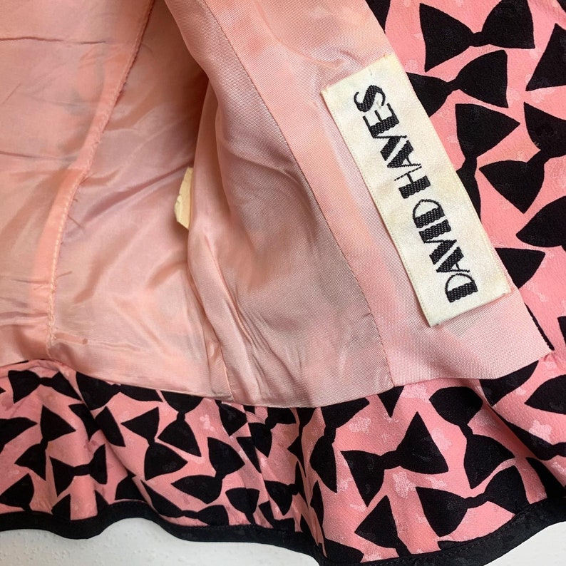 May include: Pink fabric with a black bow pattern. The fabric has a label that says "David Hayes".