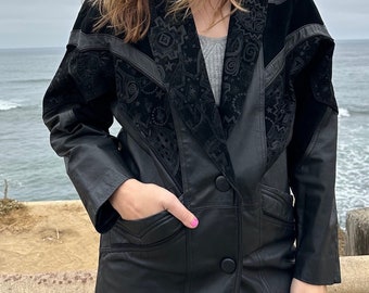 May include: A black leather jacket with a velvet collar and geometric pattern. The jacket has a single button closure and two pockets.