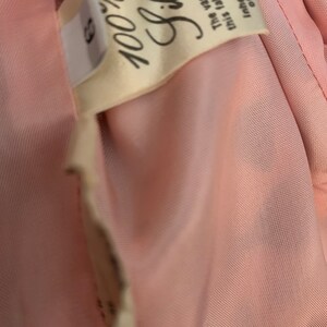 May include: A close-up of a pink fabric label with the text "100% Silk" and the following text: "The variations in this fabric are part of the inherent beauty of pure silk."