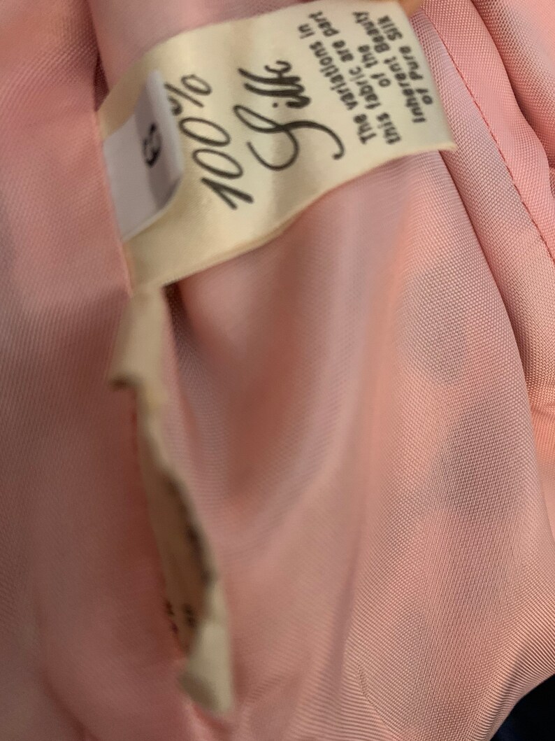 May include: A close-up of a pink fabric label with the text "100% Silk" and the following text: "The variations in this fabric are part of the inherent beauty of pure silk."