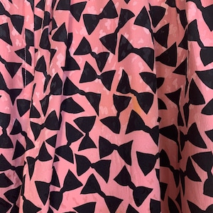 May include: Pink fabric with a black bow tie pattern. The fabric is soft and has a subtle sheen.