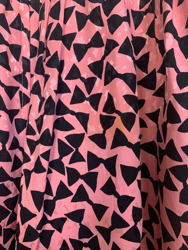 May include: Pink fabric with a black bow tie pattern. The fabric is soft and has a subtle sheen.