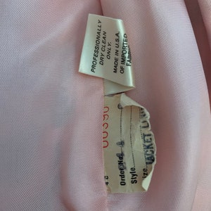 May include: Close-up of a pink fabric label with the text "Professionally Dry Clean Only. Made in U.S.A. Of Imported Fabric" and a white label with the text "Order No. 4 Style. Size Jacket Lining 00390 4C".