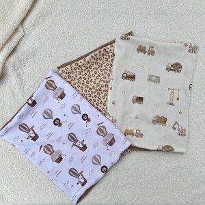 May include: Three fabric baby burp cloths with different patterns. One has a brown and white leopard print, one has a white background with brown trucks and construction vehicles, and one has a white background with brown hot air balloons and animals.