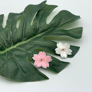 May include: Two embroidered flower patches, one pink and one white, on a green leaf.