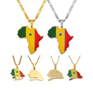 Puede incluir: Dos collares con colgantes en forma de África con la bandera de Senegal en verde, amarillo y rojo con una estrella verde. Debajo, cuatro colgantes: uno con la bandera y texto, dos mapas en tono dorado y uno con la bandera.