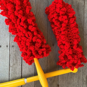 May include: Two red fluffy dusters with yellow handles. The dusters are made of yarn and are attached to the handles with a metal ring.