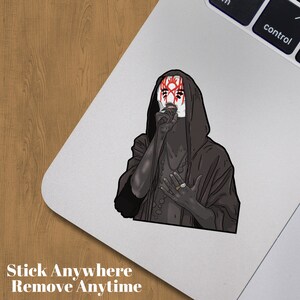 May include: A sticker depicting a figure in a black hooded robe and a white mask with red markings. The sticker has the text "Stick Anywhere Remove Anytime" at the bottom.