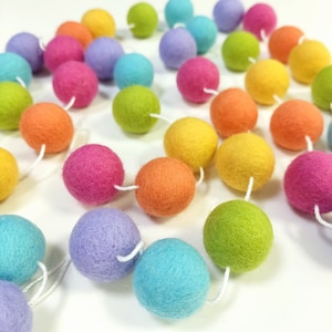 Funkelnde Regenbogengirlande aus Filzkugeln mit mehrfarbigen Pompons aus Merinowolle zur Dekoration von Schlafzimmern oder Partys.
